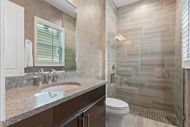a bathroom with a granite countertop sink a toilet a mirror and shower