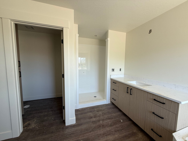 3308 South 1000 West Logan, UT 84321 - Photo 10 of 14 Spacious bathroom featuring a double vanity with stone countertops, integrated sink, wood-finish cabinetry, and matte black hardware
