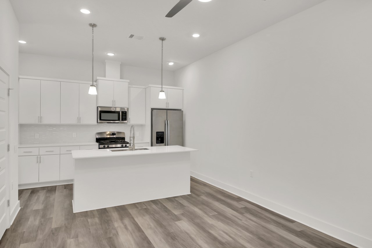 6325 Ponca Street, Unit B Austin, TX 78741 - Photo 3 of 29 Kitchen with stainless steel appliances, white cabinets, a kitchen island with sink, and hanging light fixtures