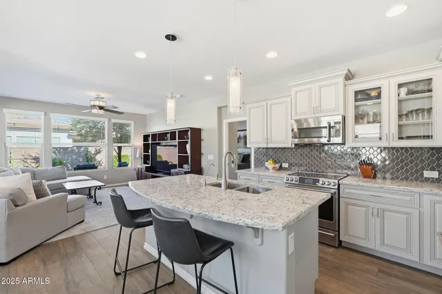 a kitchen with stainless steel appliances kitchen island granite countertop a stove a sink a refrigerator and white cabinets with wooden floor