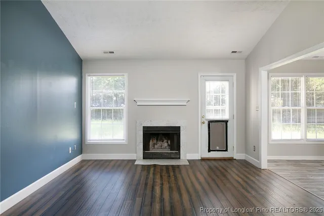 an empty room with wooden floor fireplace and windows