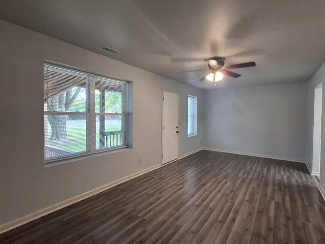an empty room with wooden floor chandelier fan and windows
