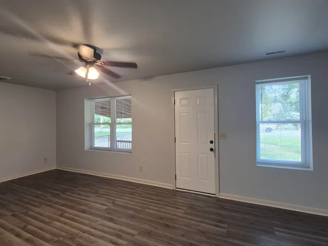an empty room with wooden floor ceiling fan and windows