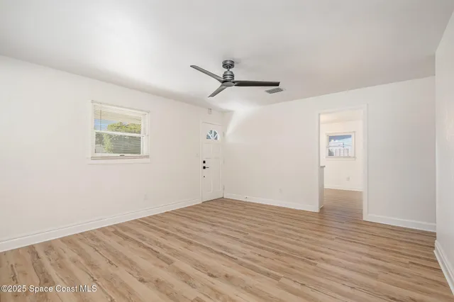 an empty room with wooden floor ceiling fan and windows