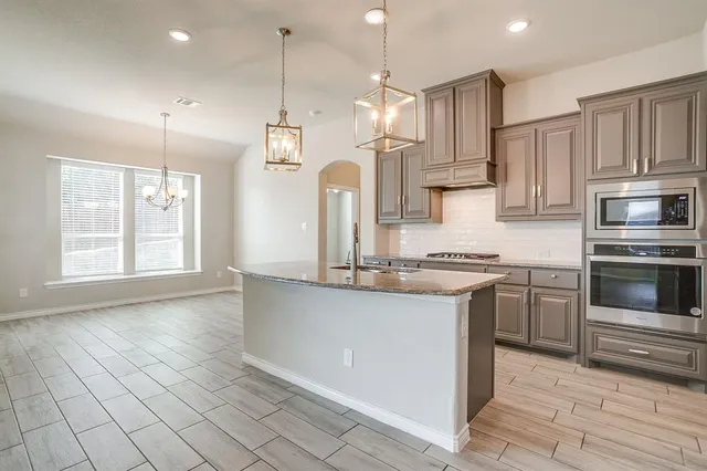 a kitchen with stainless steel appliances granite countertop a sink a stove a refrigerator and island with wooden floor