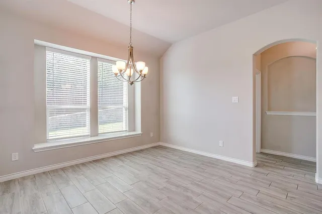 an empty room with wooden floor chandelier and windows