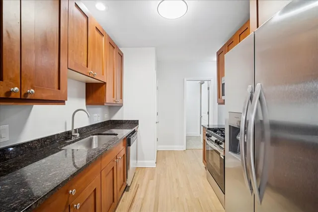 a kitchen with stainless steel appliances granite countertop a refrigerator a stove and a sink with wooden floor