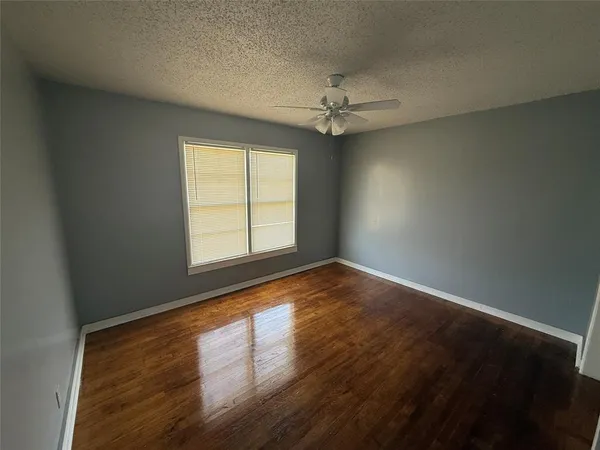 an empty room with wooden floor fan and windows