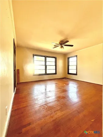 a view of empty room with wooden floor and fan
