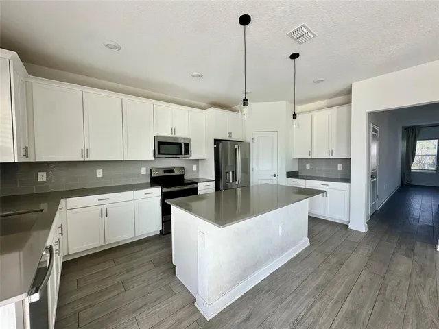 a large kitchen with stainless steel appliances granite countertop a stove a sink and white cabinets with wooden floor