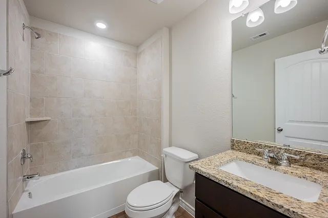 a bathroom with a granite countertop sink toilet vanity mirror bathtub and shower