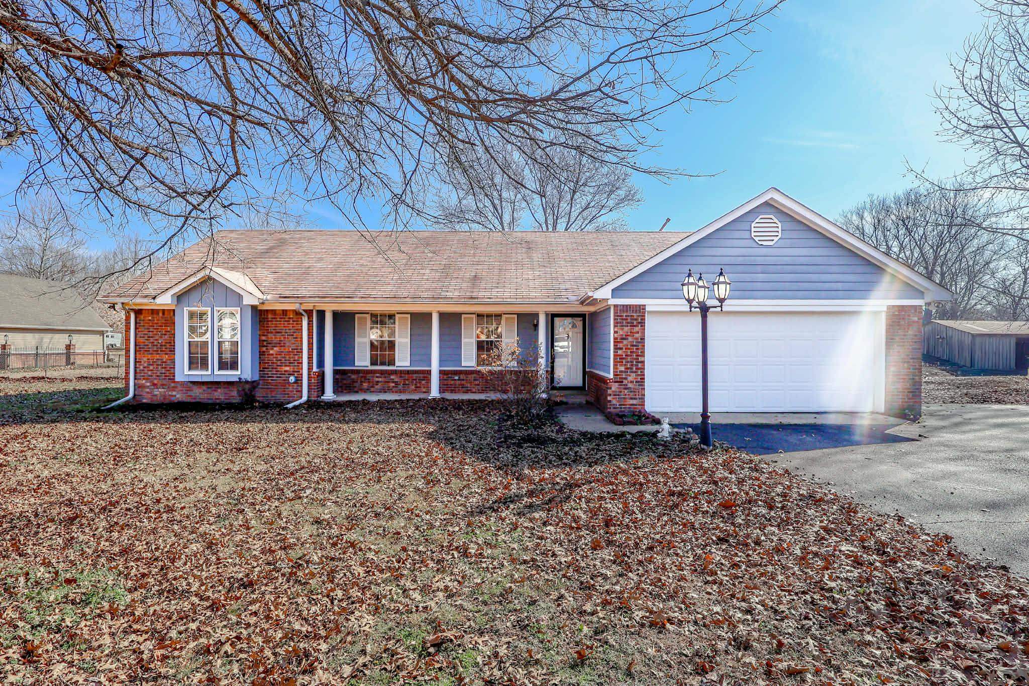 Ranch-style house with covered porch, asphalt driveway, brick siding, a garage, and a shingled roof