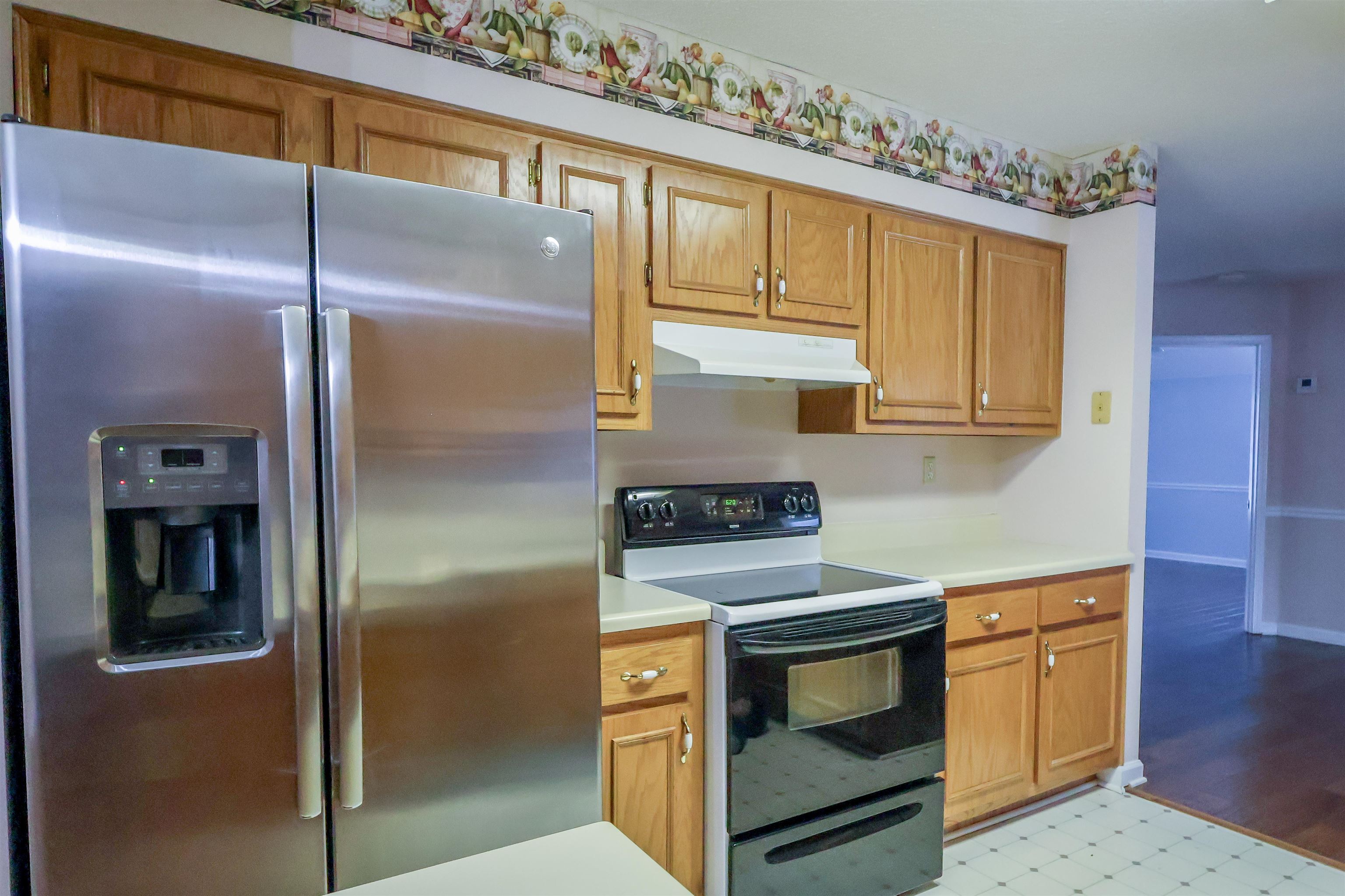 Kitchen featuring stainless steel fridge with ice dispenser, electric stove, light countertops, wood finish cabinetry, and light floors