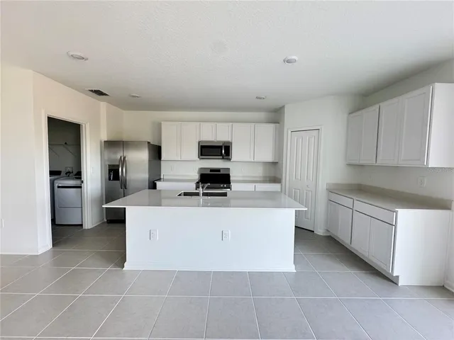 a large kitchen with stainless steel appliances a sink a stove a refrigerator a microwave and cabinets