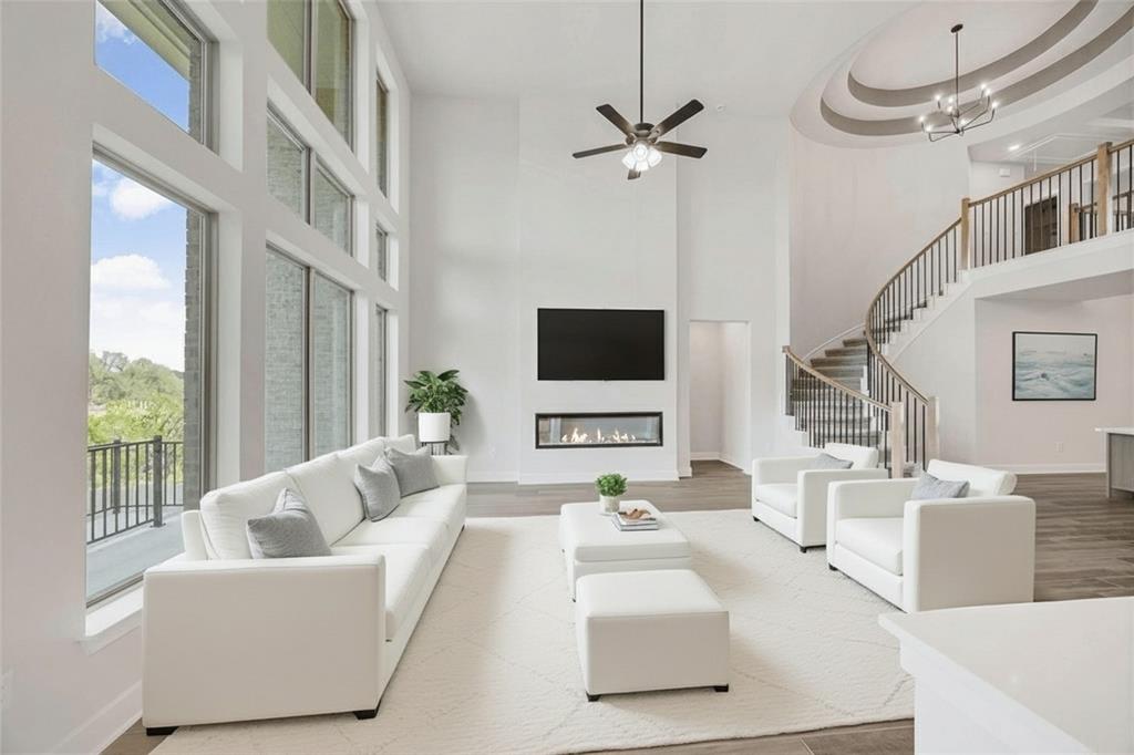 504 Sundance Ridge Georgetown, TX 78628 - Photo 5 of 34 Double-height windows illuminate the spacious living area featuring a modern fireplace and curved staircase.