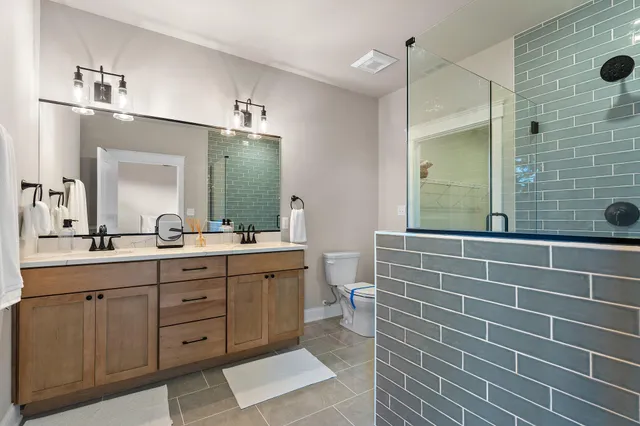 a bathroom with a double vanity sink a toilet a mirror and shower