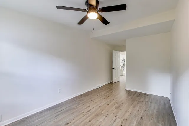 an empty room with wooden floor ceiling fan and window