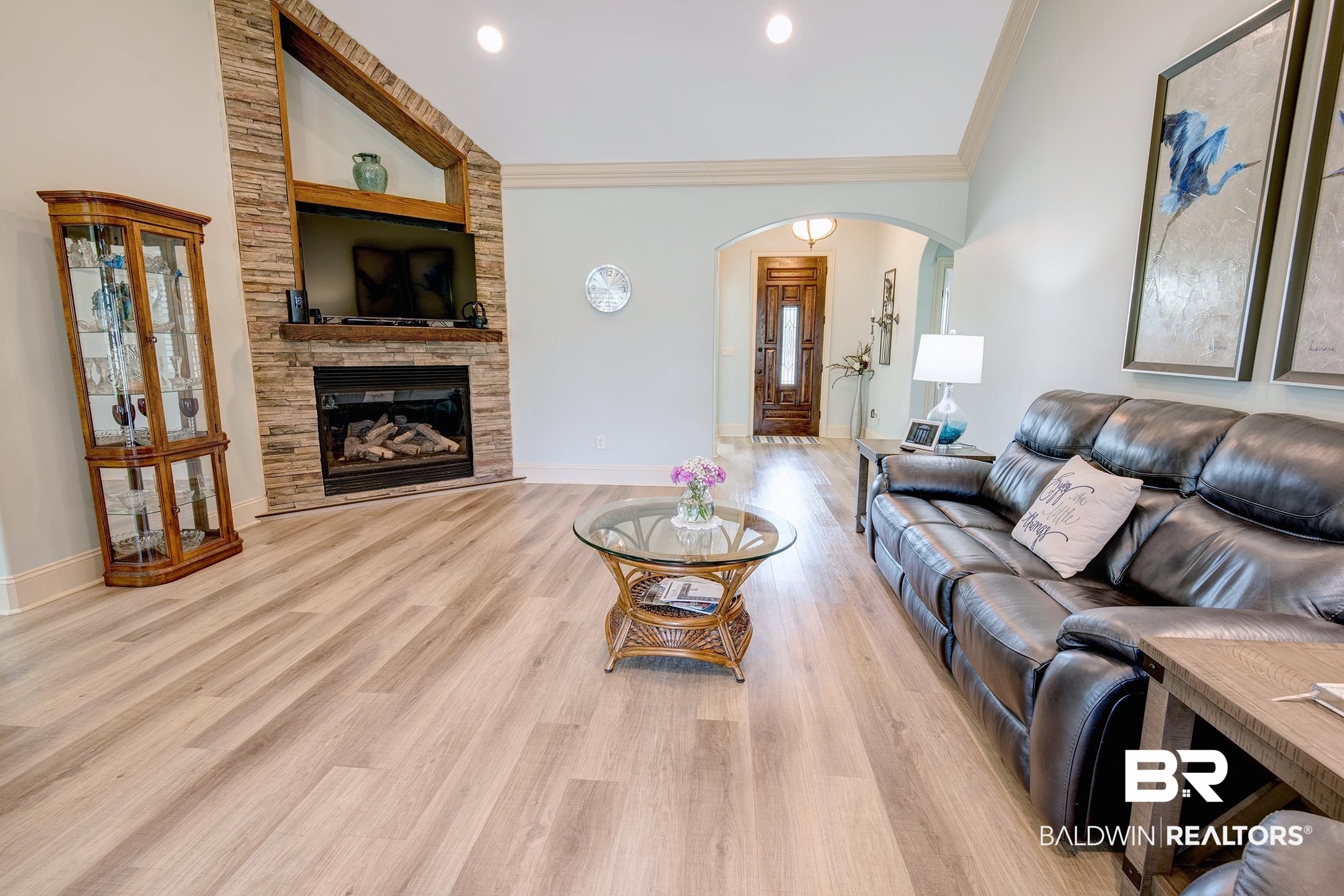 9357 Lakeview Drive Foley, AL 36535 - Photo 47 of 68 Living area featuring wood-finish flooring, a stacked stone fireplace with a wood mantle, vaulted ceilings, and an arched entry