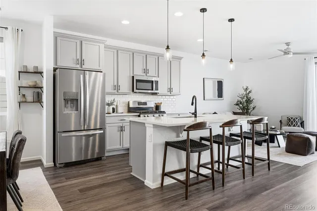 a kitchen with stainless steel appliances a refrigerator a stove a sink a dining table and chairs with wooden floor