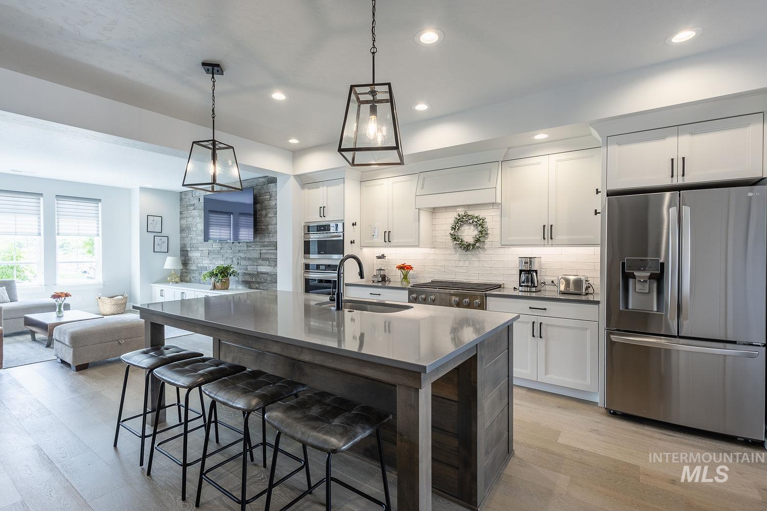 3321 South Hopes Well Way Boise, ID 83716 - Photo 11 of 40 Kitchen featuring appliances with stainless steel finishes, white cabinetry, decorative backsplash, a breakfast bar area, and decorative light fixtures