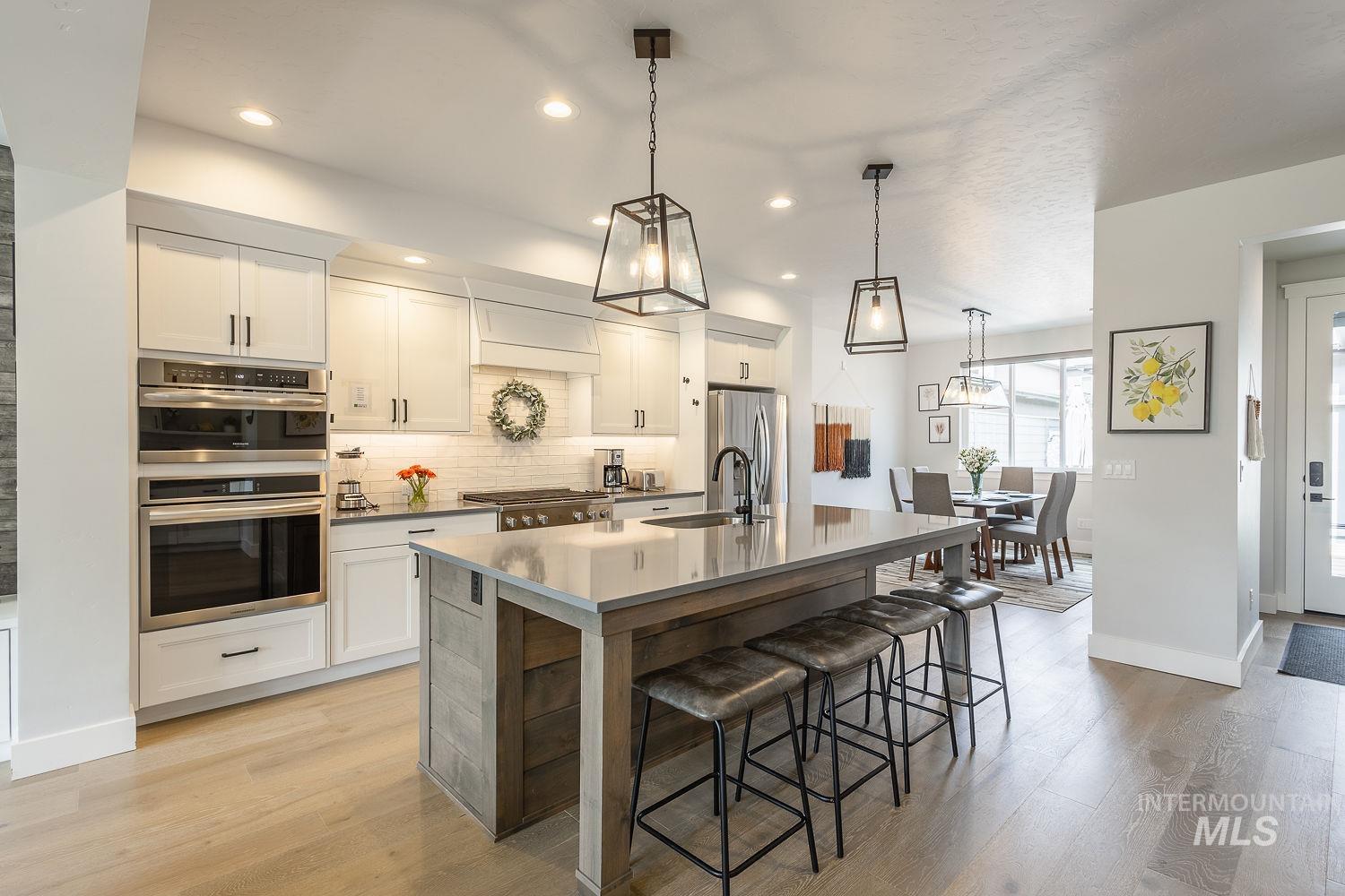3321 South Hopes Well Way Boise, ID 83716 - Photo 13 of 40 Kitchen with backsplash, white cabinets, pendant lighting, stainless steel appliances, and light wood-style flooring