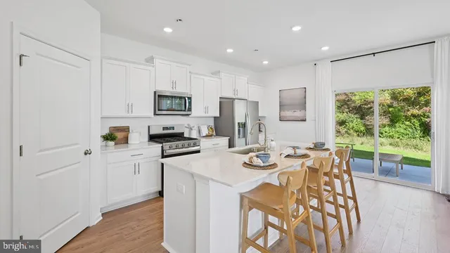 a kitchen with stainless steel appliances granite countertop a refrigerator a sink dishwasher a stove and white cabinets with wooden floor