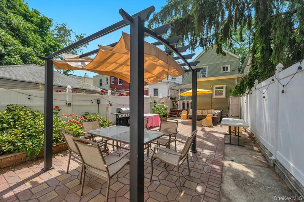 89-13 84th Street Queens, NY 11421 - Photo 8 of 34 Paved patio area featuring a pergola with retractable canvas shades, a privacy fence, and mature trees providing natural shading