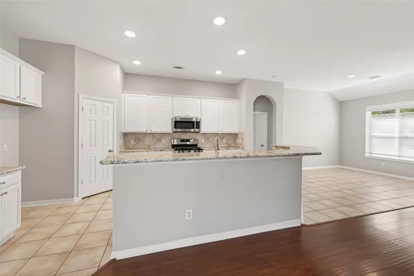 a view of kitchen with stainless steel appliances granite countertop a stove a sink a refrigerator and white cabinets with wooden floor