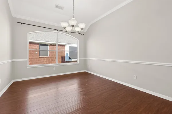 an empty room with wooden floor chandelier and windows