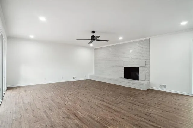 a view of an empty room with wooden floor and a ceiling fan