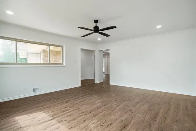 an empty room with wooden floor ceiling fan and windows