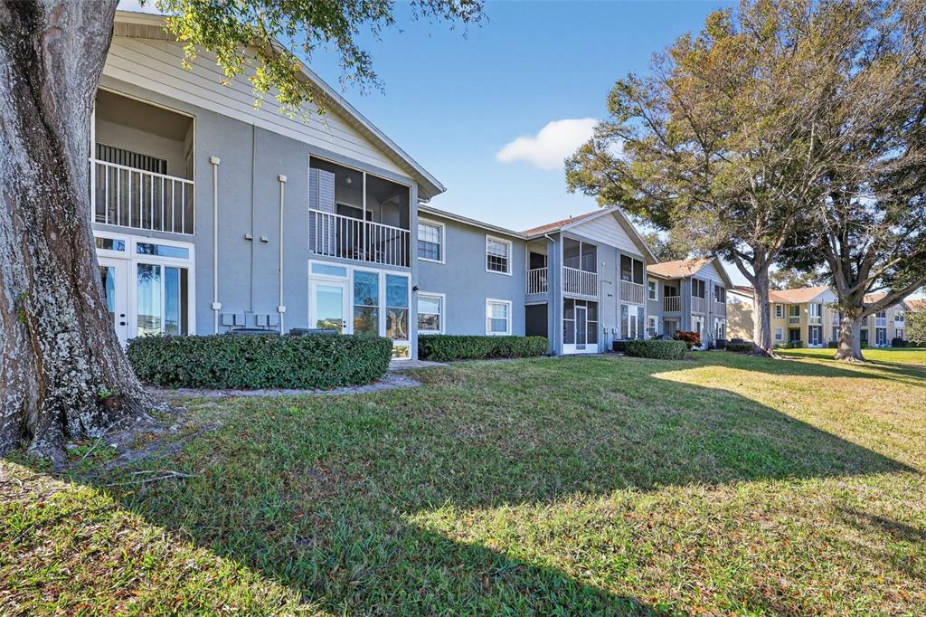 1438 Millstream Lane, Unit 105 Dunedin, FL 34698 - Photo 27 of 34 a view of a brick building next to a yard with big trees