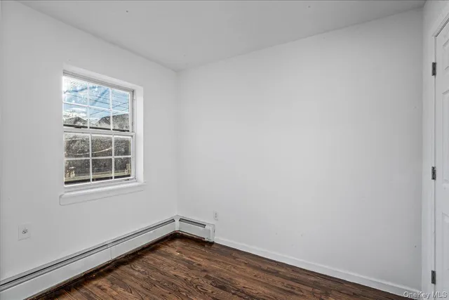 a view of an empty room with wooden floor and a kitchen