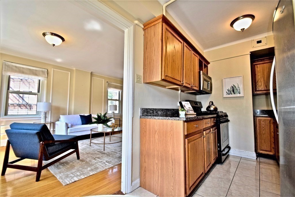 1450 Beacon Street, Unit 342 Brookline, MA 02446 - Photo 5 of 16 a living room with stainless steel appliances kitchen island granite countertop a refrigerator a stove a sink and a dining table with wooden floor