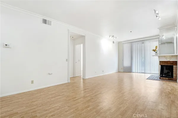 a view of an empty room with wooden floor fireplace and a window