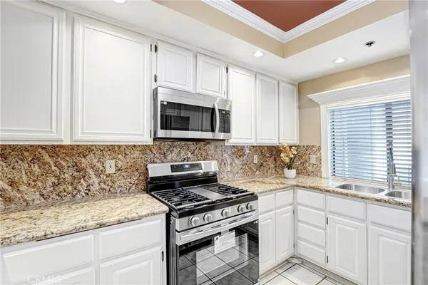 a kitchen with granite countertop white cabinets appliances and a window