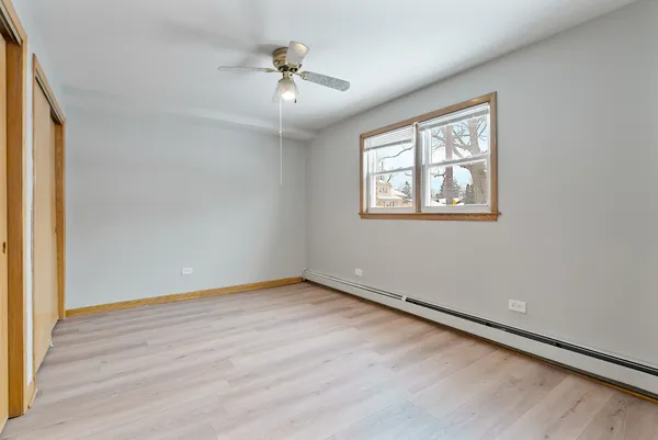 an empty room with wooden floor chandelier fan and windows