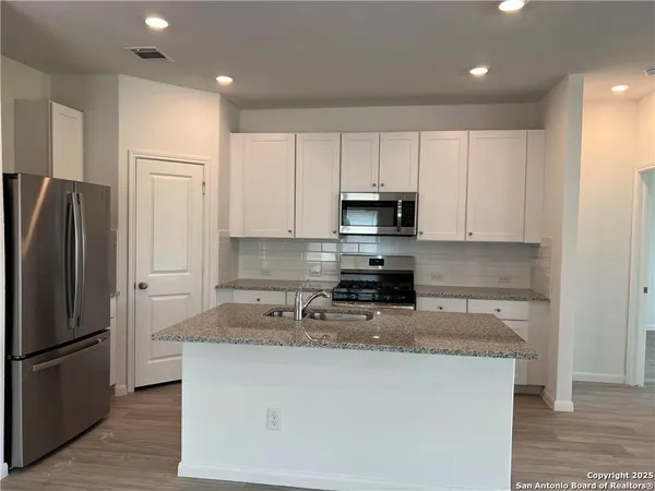 a kitchen with kitchen island granite countertop a refrigerator a sink a stove a microwave and island