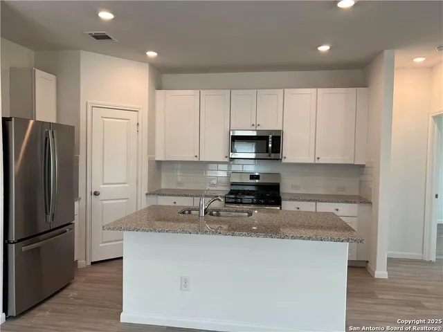 a kitchen with kitchen island granite countertop a refrigerator a sink a stove a microwave and island