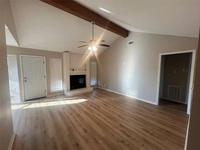 a view of an empty room with wooden floor and a ceiling fan