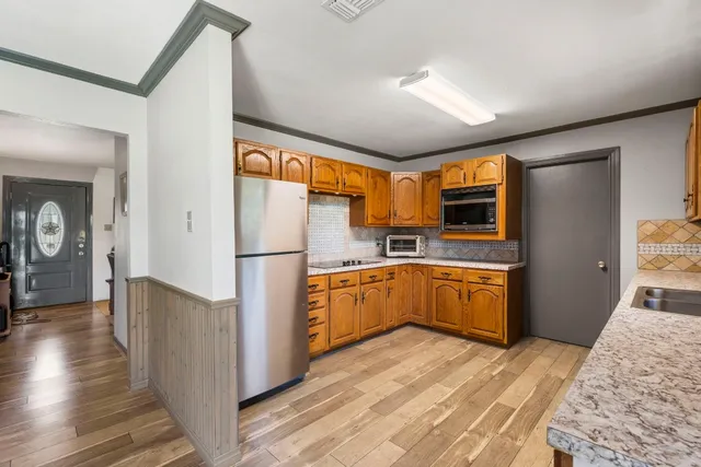 a kitchen with stainless steel appliances granite countertop a refrigerator a sink dishwasher a stove with wooden cabinets and floors