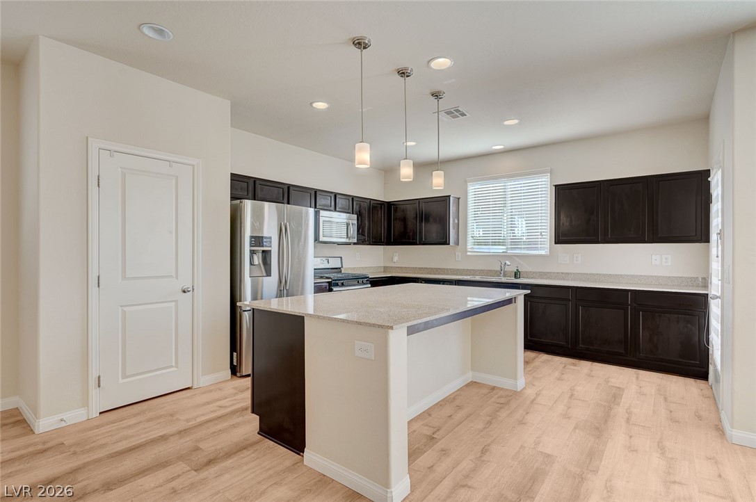 113 Elm Reed Avenue Las Vegas, NV 89113 - Photo 17 of 62 Kitchen featuring pendant lighting, stainless steel appliances, light wood-style floors, a kitchen island, and light stone countertops