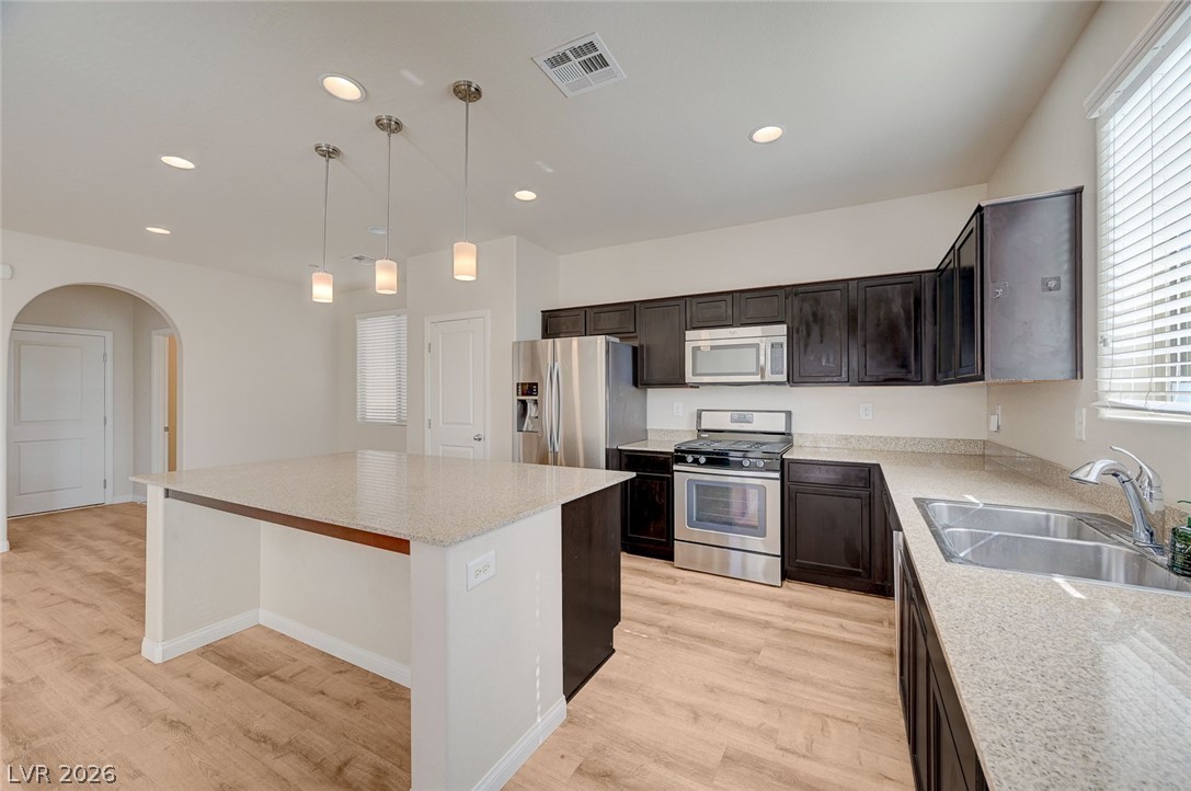 113 Elm Reed Avenue Las Vegas, NV 89113 - Photo 19 of 62 Kitchen featuring arched walkways, stainless steel appliances, light stone countertops, light wood-style flooring, and decorative light fixtures