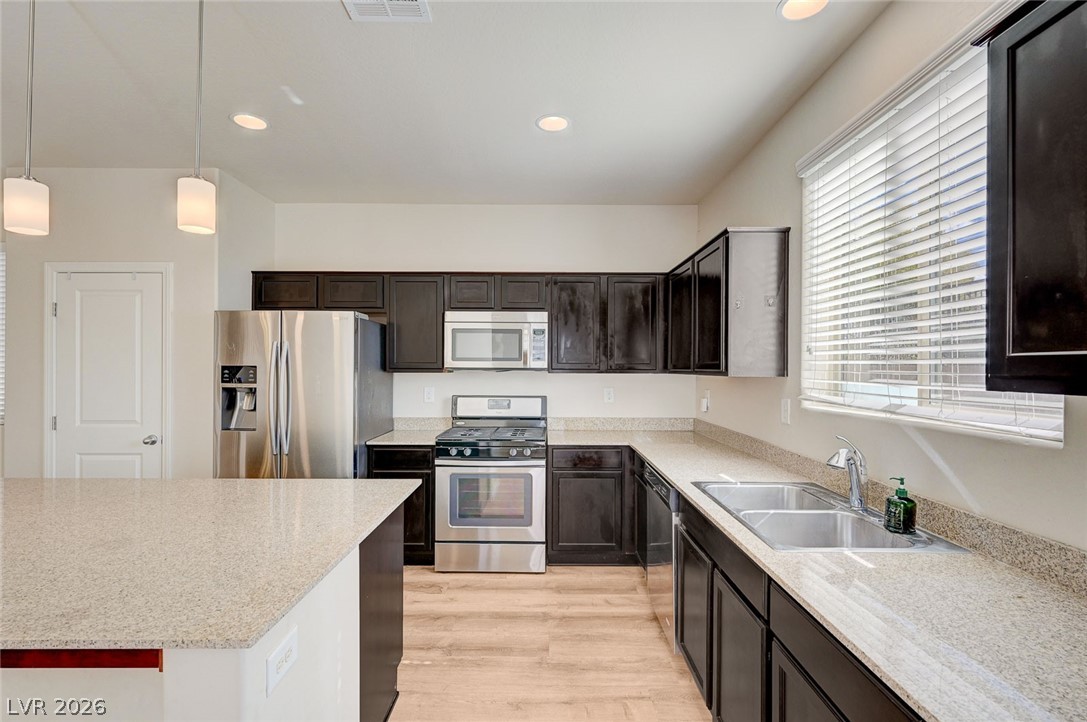 113 Elm Reed Avenue Las Vegas, NV 89113 - Photo 20 of 62 Kitchen featuring stainless steel appliances, pendant lighting, light wood-style flooring, light stone countertops, and dark wood finish cabinetry