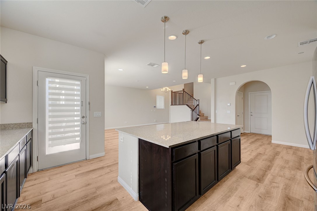 113 Elm Reed Avenue Las Vegas, NV 89113 - Photo 21 of 62 Kitchen featuring a kitchen island, arched walkways, pendant lighting, light stone counters, and light wood-style floors
