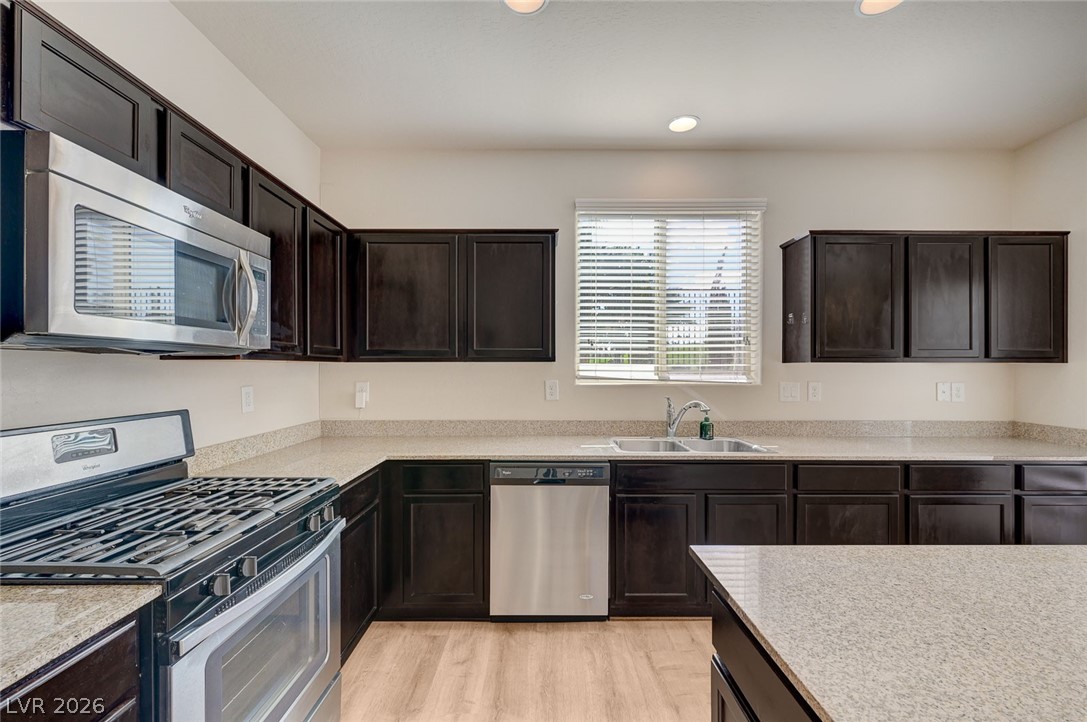 113 Elm Reed Avenue Las Vegas, NV 89113 - Photo 22 of 62 Kitchen with stainless steel appliances, dark wood finish cabinets, light wood finished floors, and light stone countertops