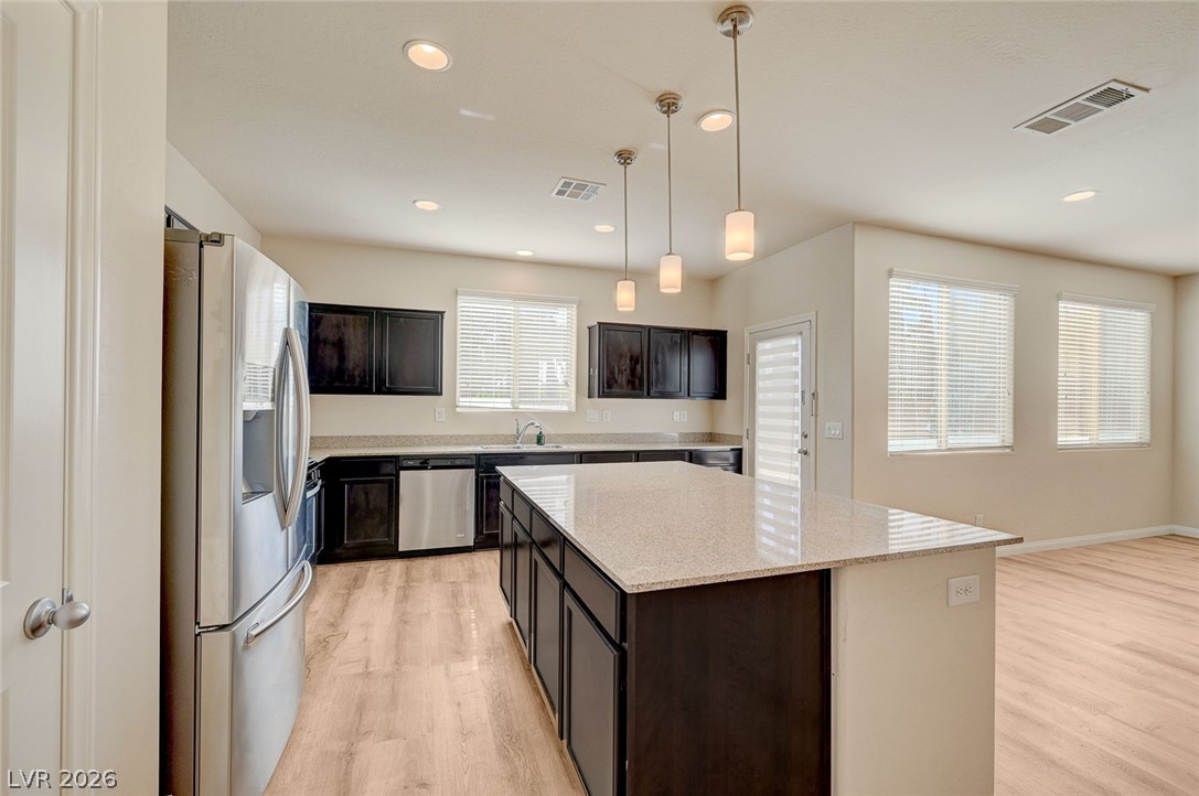 113 Elm Reed Avenue Las Vegas, NV 89113 - Photo 23 of 62 Kitchen featuring stainless steel appliances, light wood finished floors, pendant lighting, light stone countertops, and a kitchen island