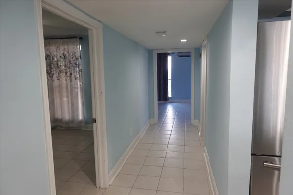 an empty room with chandelier fan and kitchen view