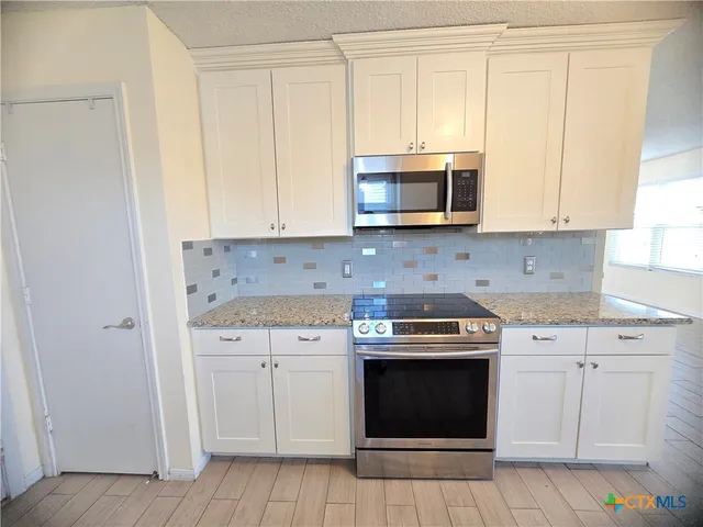 a kitchen with granite countertop white cabinets and stainless steel appliances
