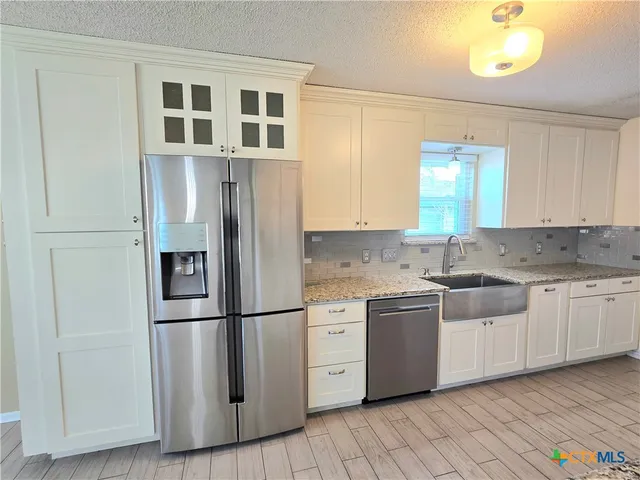 a kitchen with stainless steel appliances granite countertop a refrigerator a sink and white cabinets with wooden floor